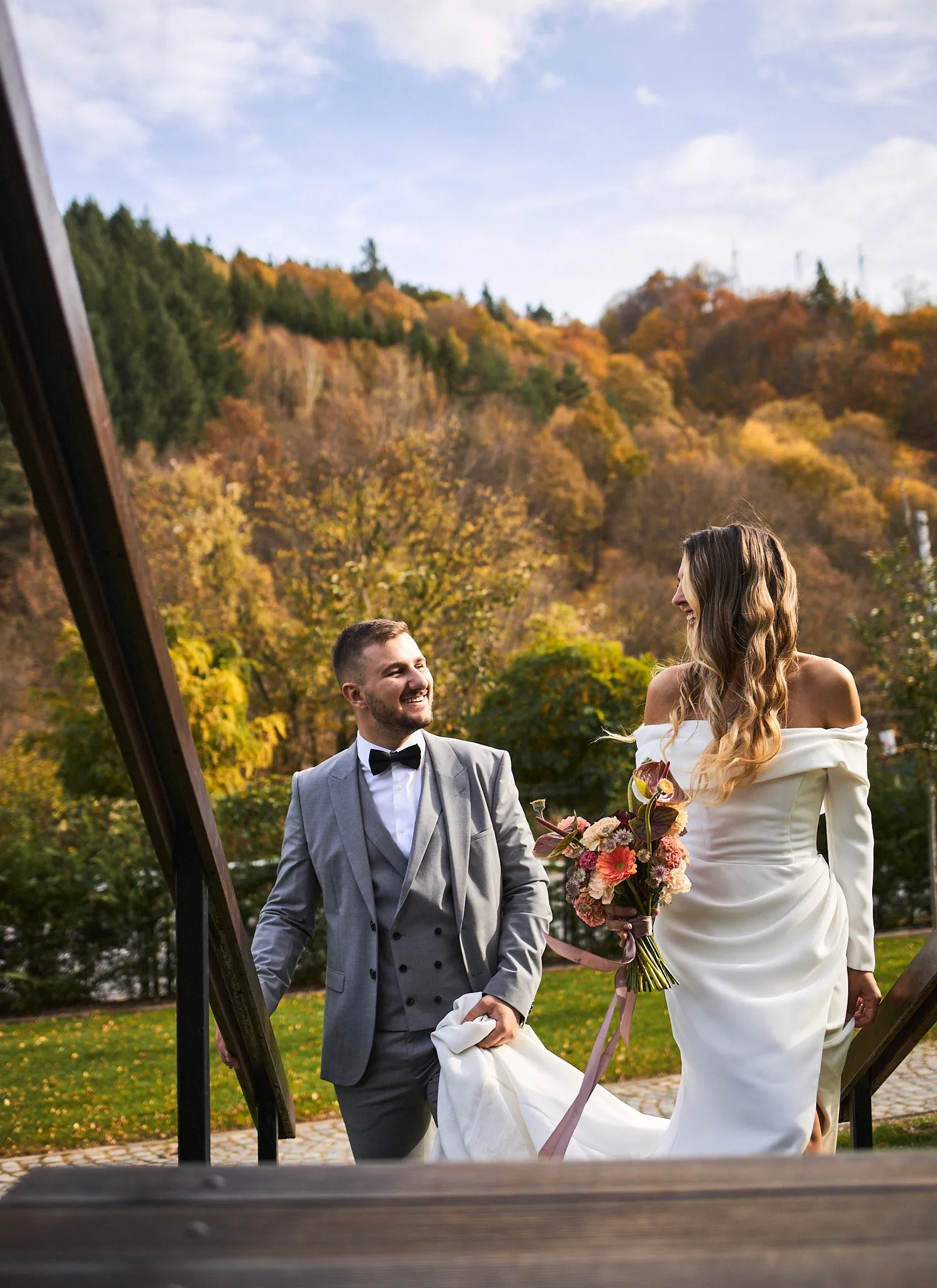 Bride and groom laughing as they climb wooden stairs, autumn hills behind them