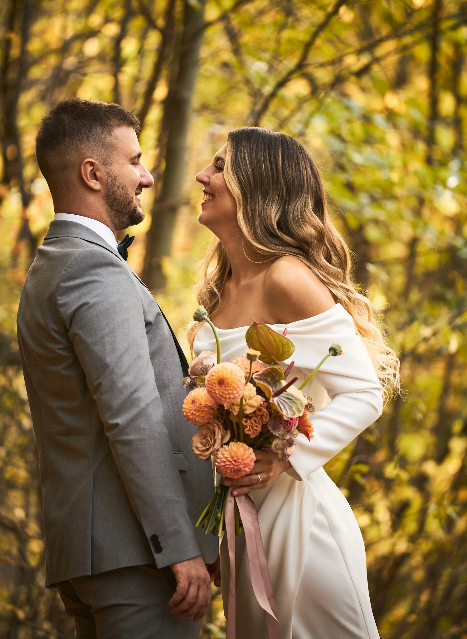 Bride with a peach-toned bouquet laughing with the groom in an autumn forest