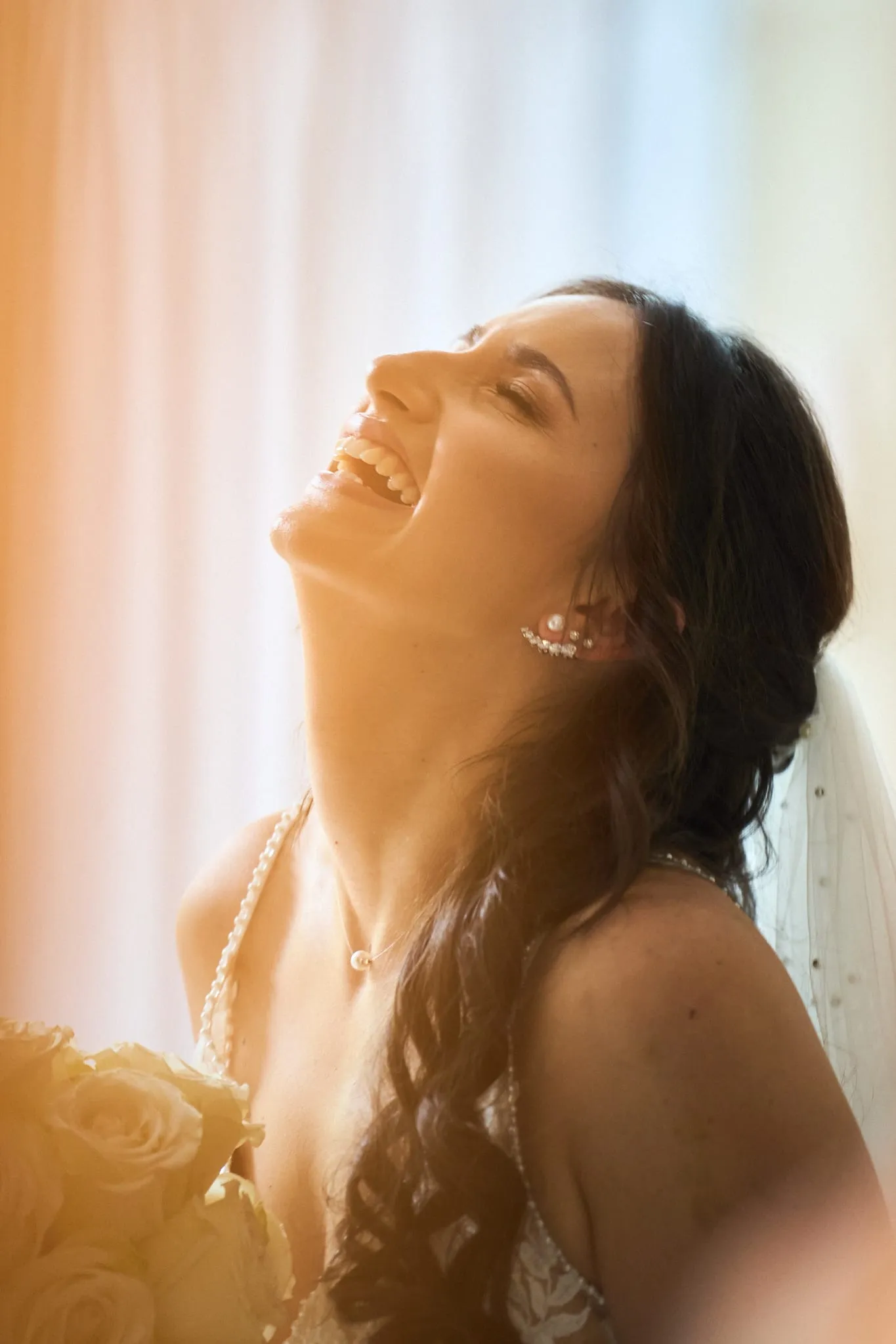 Bride laughing with her eyes closed in warm window light