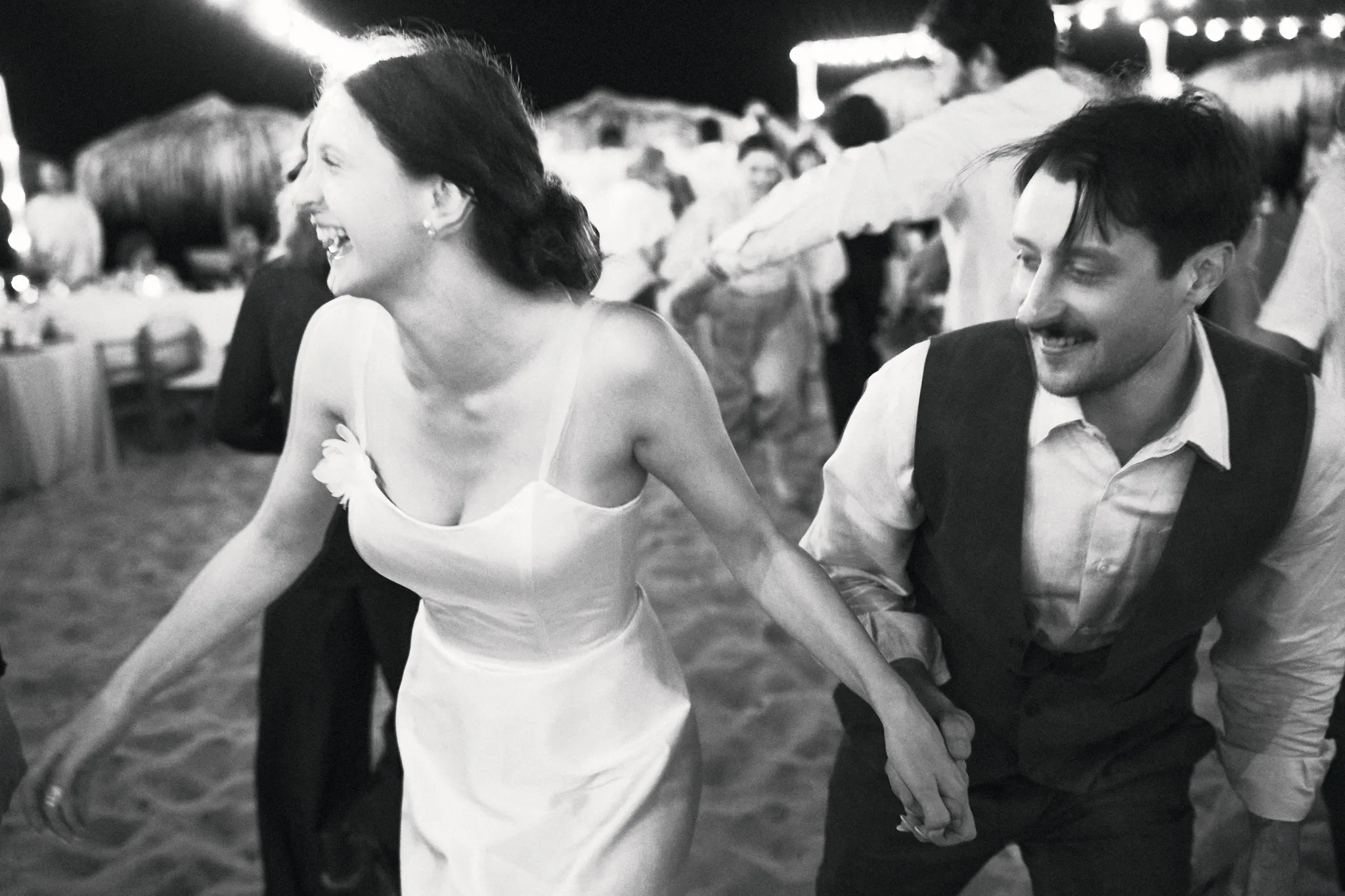 Black-and-white photo of the couple dancing among guests on the beach